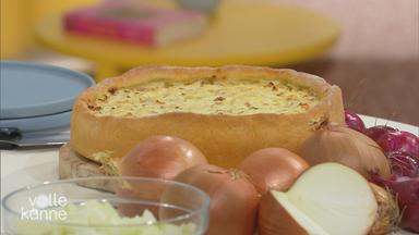 Zwiebelkuchen auf einem Tisch zu sehen, davor Zwiebeln.