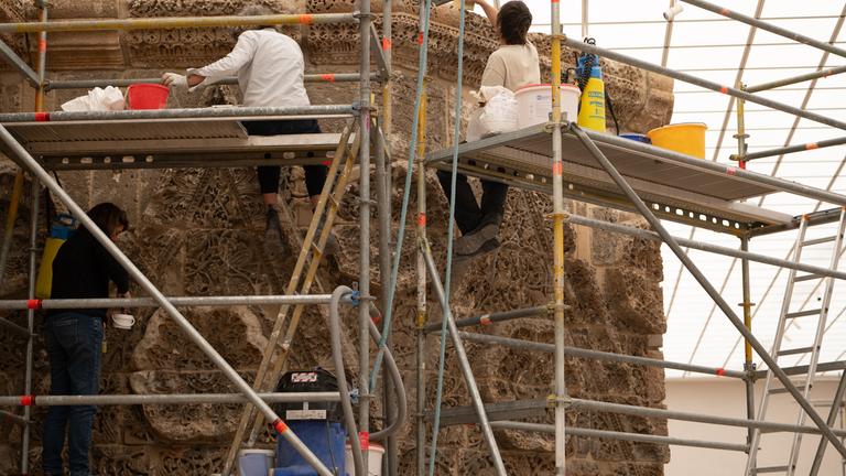 Menschen arbeiten an den Fugen der Mschatta-Fassade. 